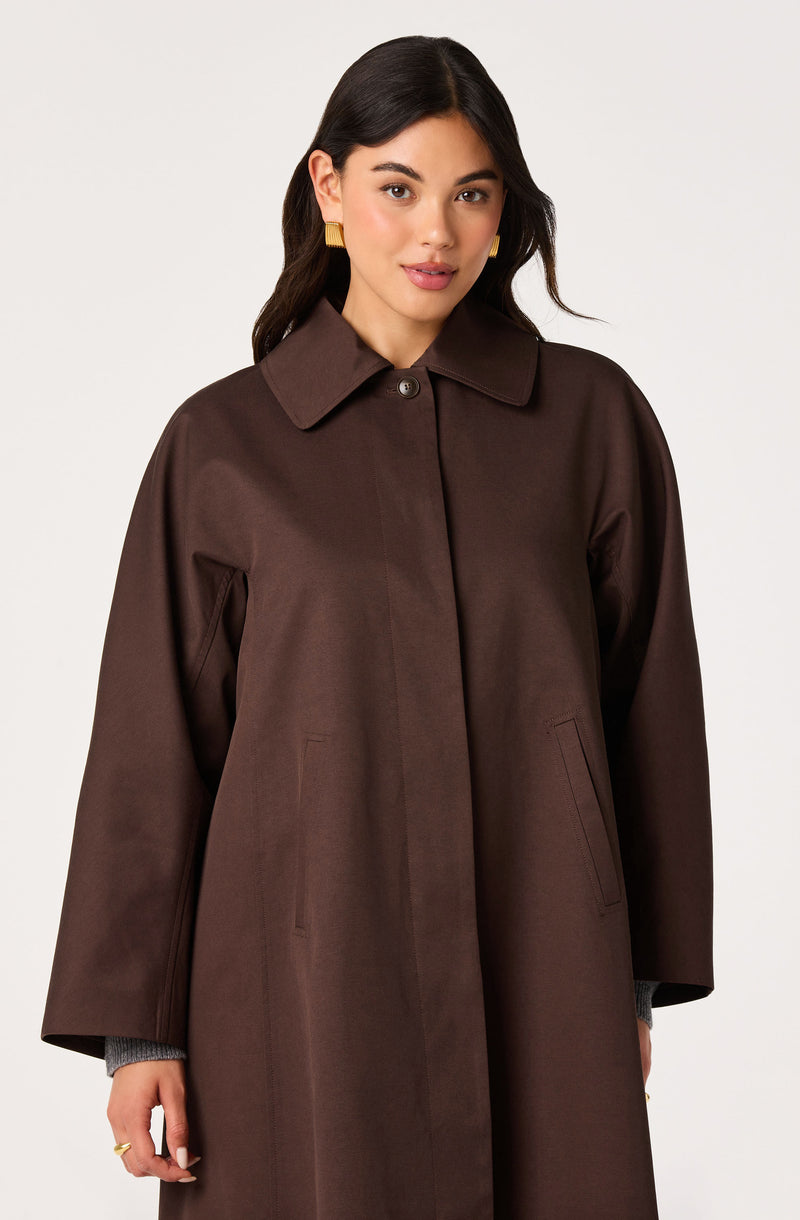 Woman wearing a long, dark brown coat with a classic collar and front pockets.