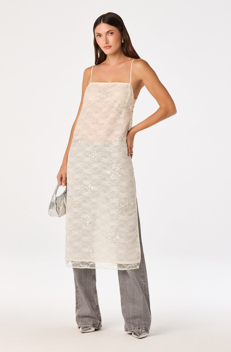 Woman wearing a nude slip dress layered over a sheer lace dress with floral embroidery.
