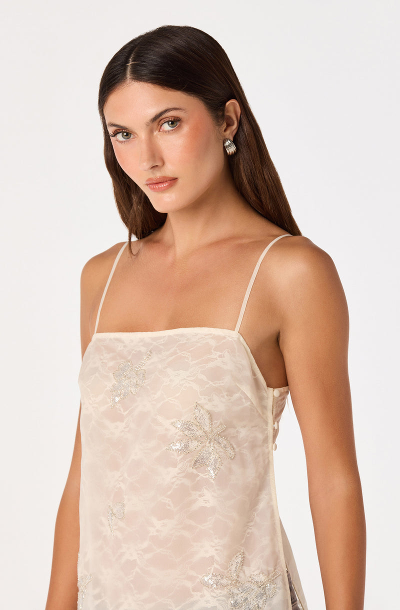 Woman in a cream satin slip dress with floral embroidery and thin spaghetti straps.