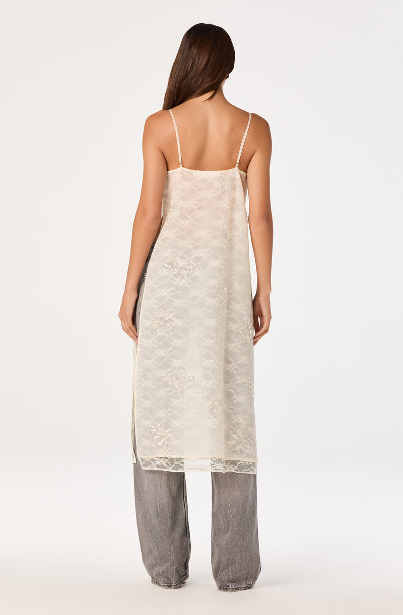 Cream-colored slip dress with thin spaghetti straps layered over gray wide-leg pants.
