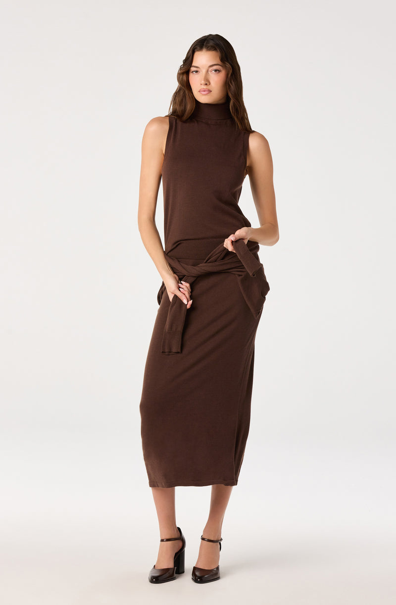 Woman wearing a sleeveless brown turtleneck top and a matching long skirt with a tied waist.