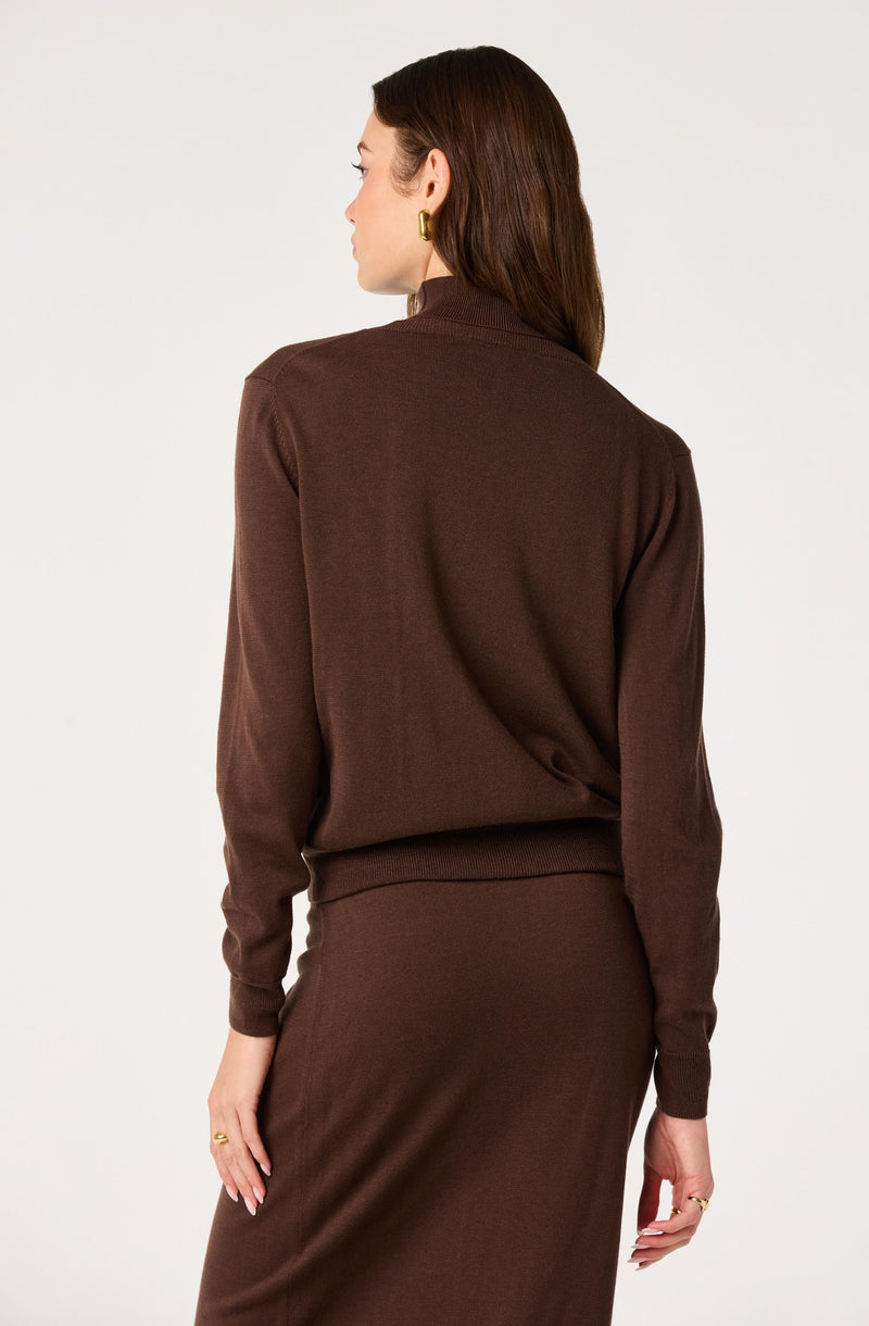 Woman wearing a brown long-sleeve sweater and matching skirt, facing away.