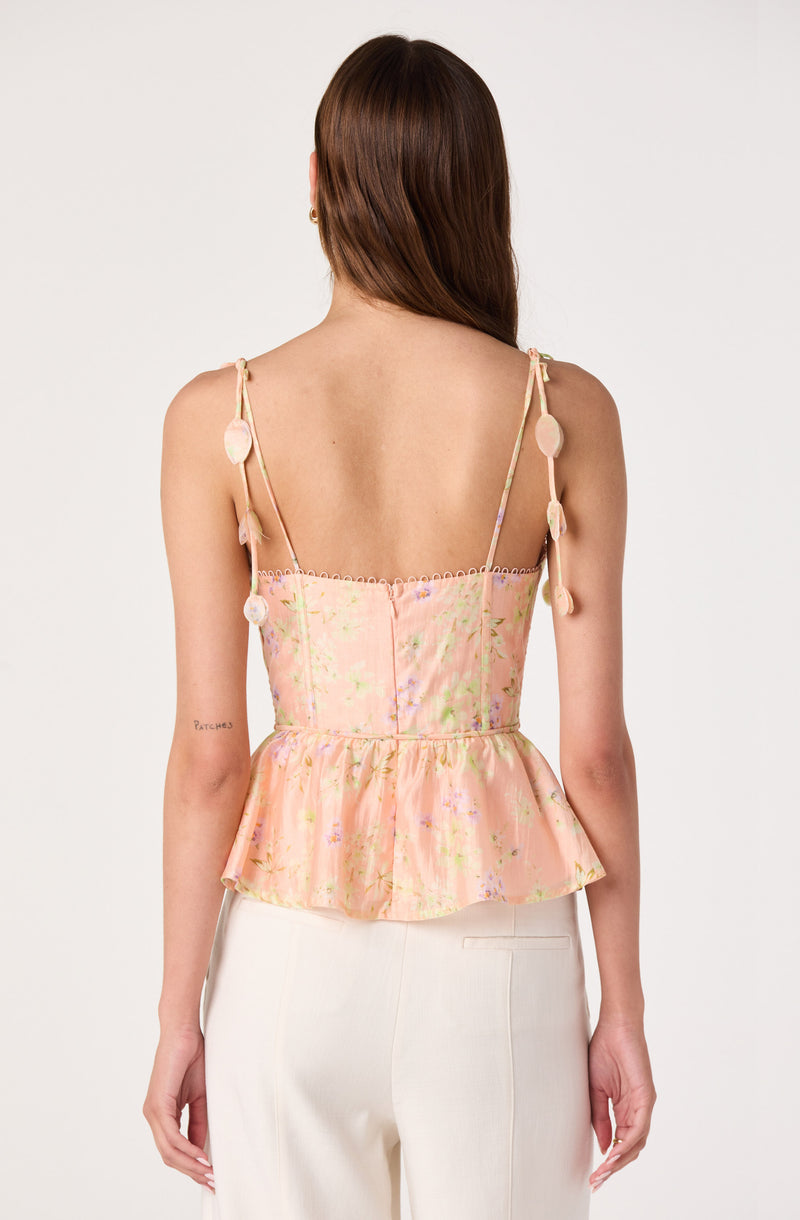 Pink floral sleeveless top with pom-pom shoulder details and ruffled hem.