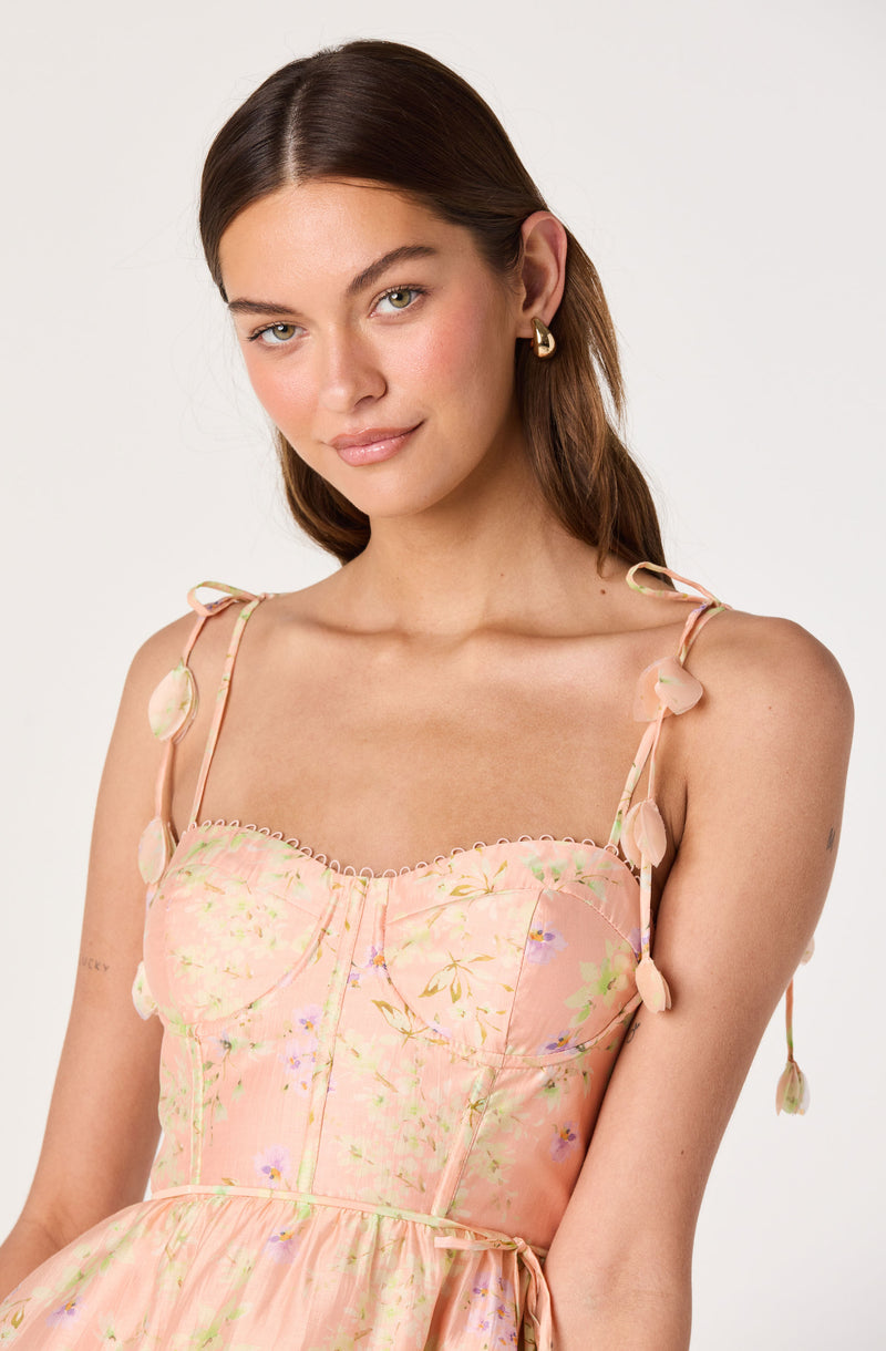 Woman wearing a peach-colored dress with floral patterns and decorative shoulder ties.