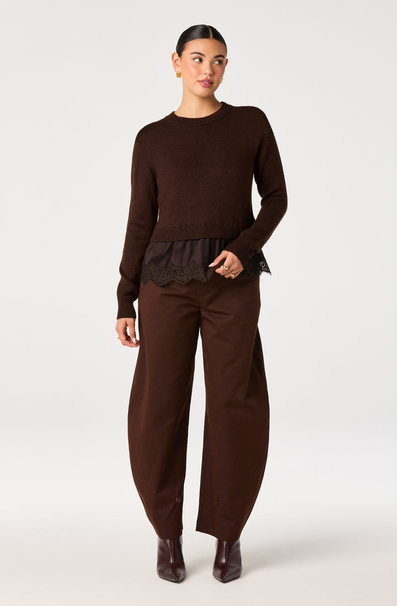 Woman wearing a brown sweater with layered black lace trim, brown wide-leg pants, and matching ankle boots.