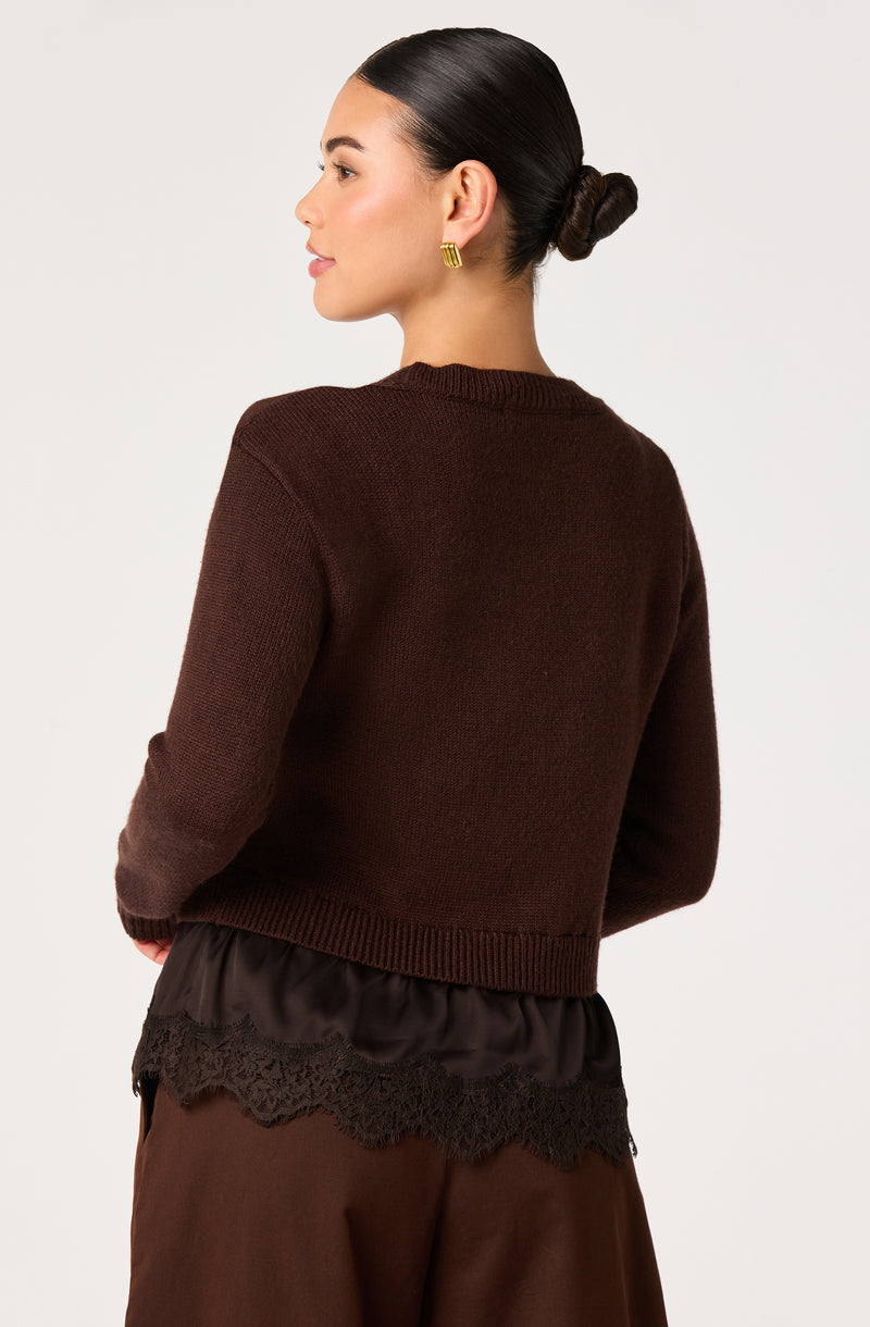 Woman in brown sweater with a black lace-trimmed hem, wearing gold earrings, side profile view.