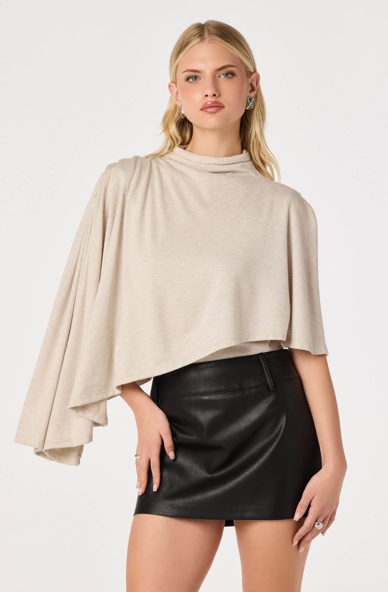 Beige cape top with draped sleeve paired with a black leather mini skirt.