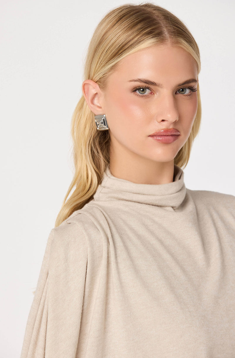 Woman in beige turtleneck with square silver earrings.