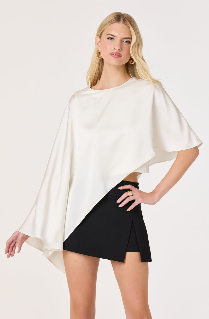 Woman wearing a white asymmetrical top with wide sleeves and a black mini skirt with a slit.