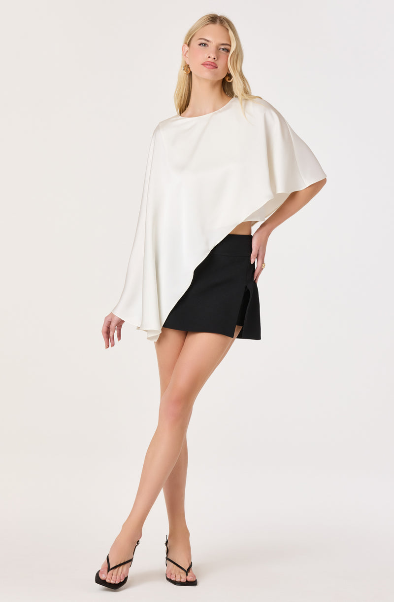 Woman wearing a loose white top with bell sleeves and a black mini skirt with a side slit.