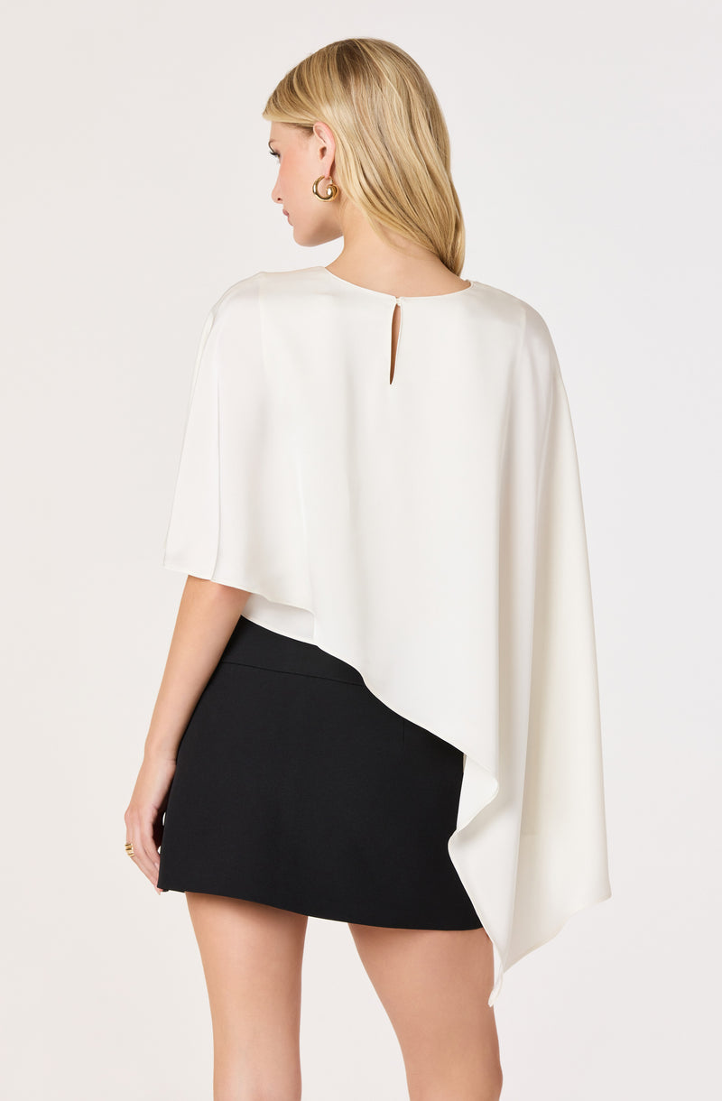 Woman wearing a white asymmetrical top with a keyhole back and a black mini skirt.