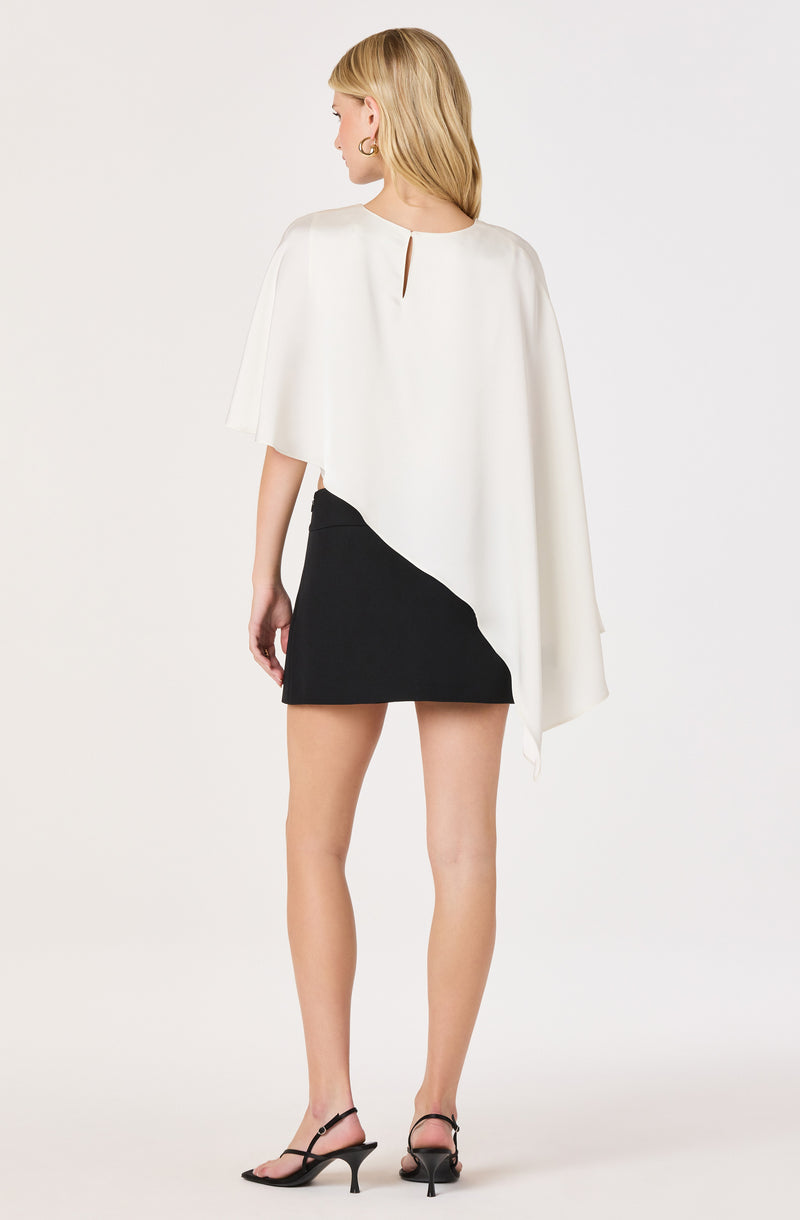 Woman wearing a white cape-style top and a black color-block mini skirt.