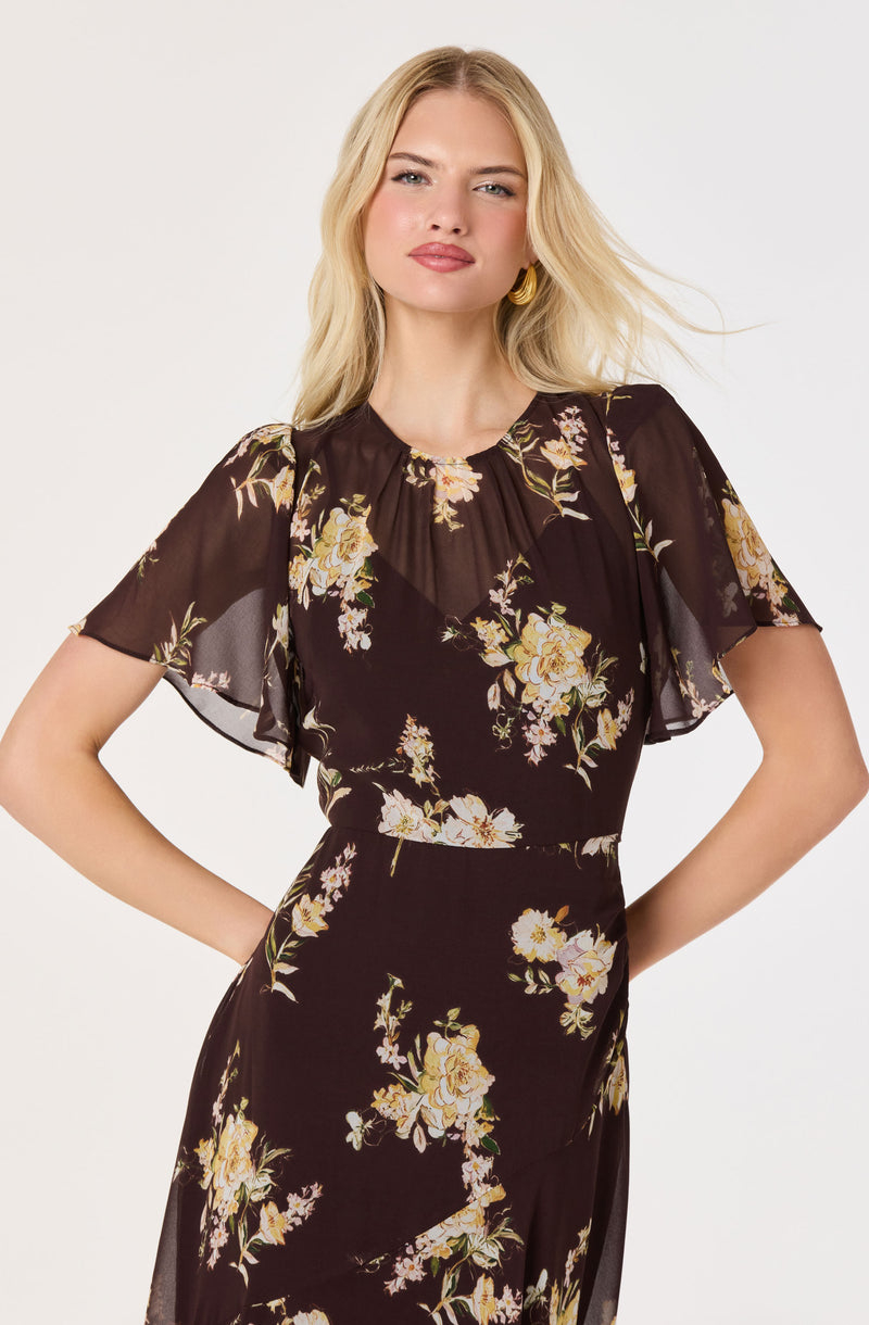 Woman wearing a black floral dress with sheer flutter sleeves.