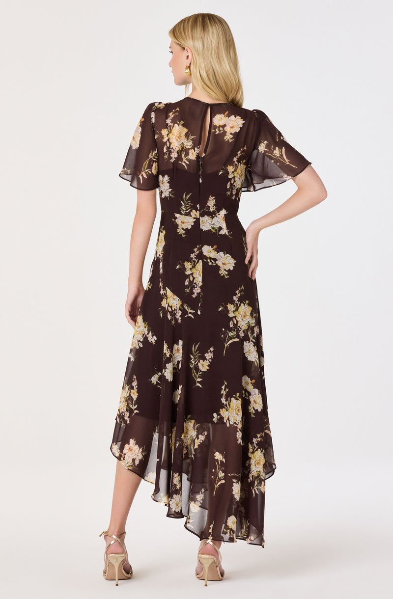 Woman in a long, dark floral dress with short, sheer sleeves and open back, wearing high heels.