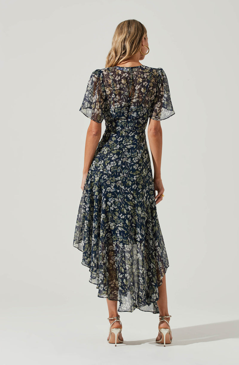 Woman wearing a sheer black floral dress with puffed sleeves and high-low hemline.