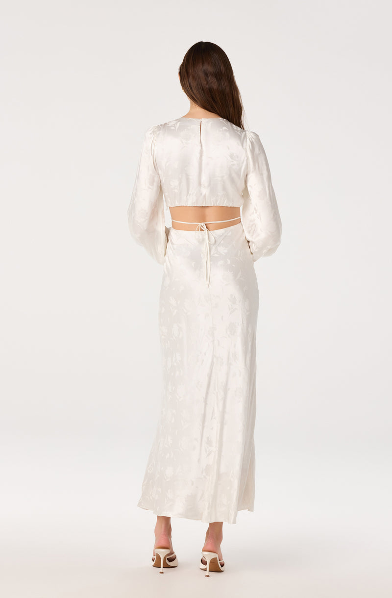 Woman in a long, satin, ivory dress with puffed sleeves and a cropped top with tie-back detail.