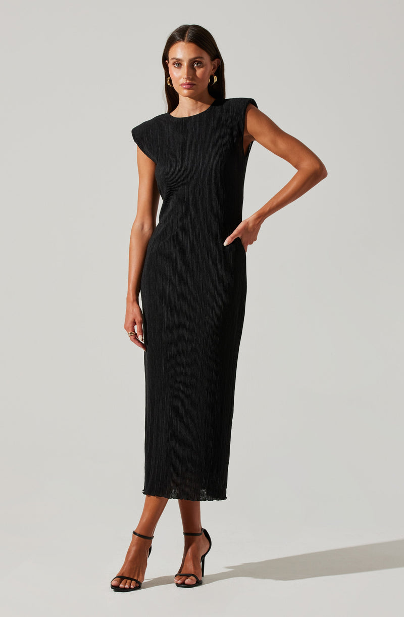 A woman is wearing a black, sleeveless, ankle-length dress with a subtle vertical ribbed texture. The dress has structured, slightly padded shoulders and a fitted silhouette. She is also wearing black high-heeled sandals with ankle straps.
