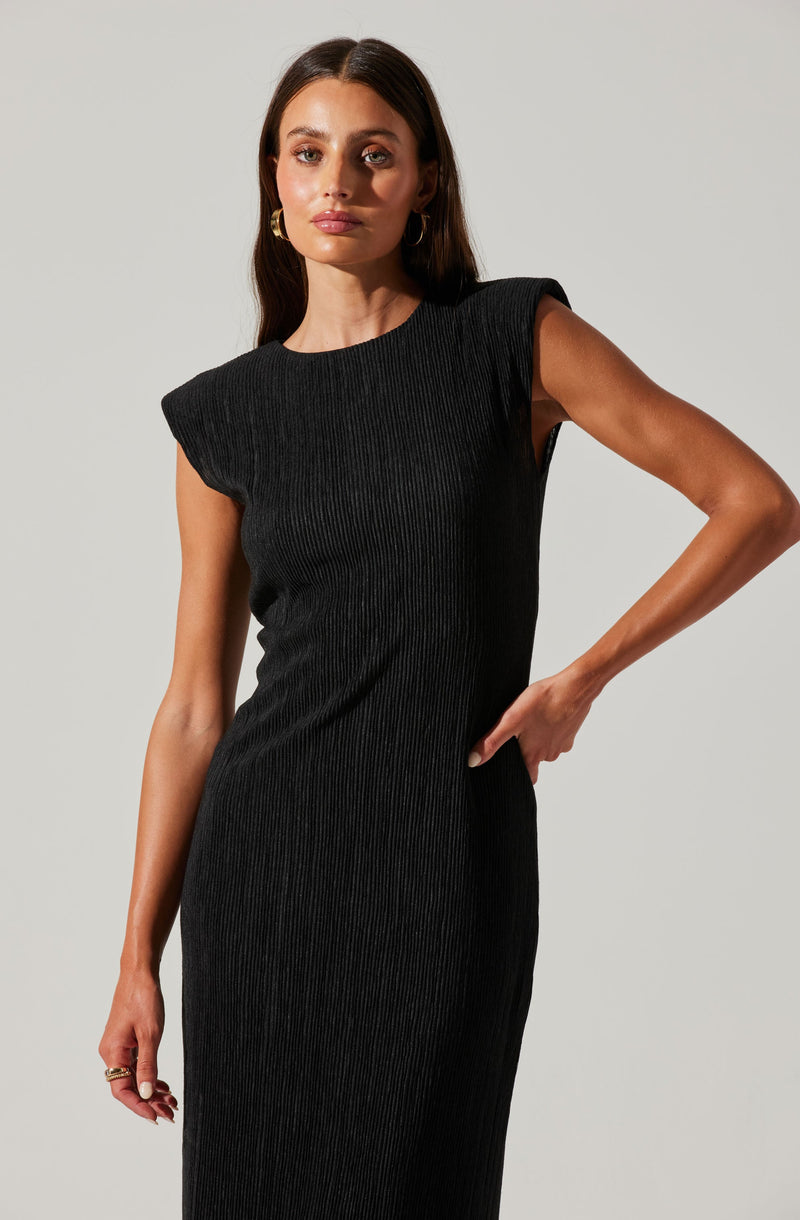 A woman is wearing a fitted, sleeveless black dress with a ribbed texture. The dress features structured shoulder details, giving it a modern and stylish appearance.