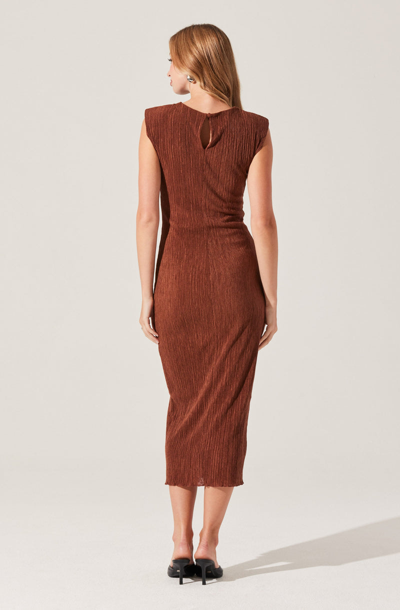 A woman is wearing a sleeveless, fitted midi dress in a rich, textured rust color. The dress features subtle vertical ribbing and a keyhole cutout at the upper back, near the neckline. She completes her look with black high-heeled shoes.