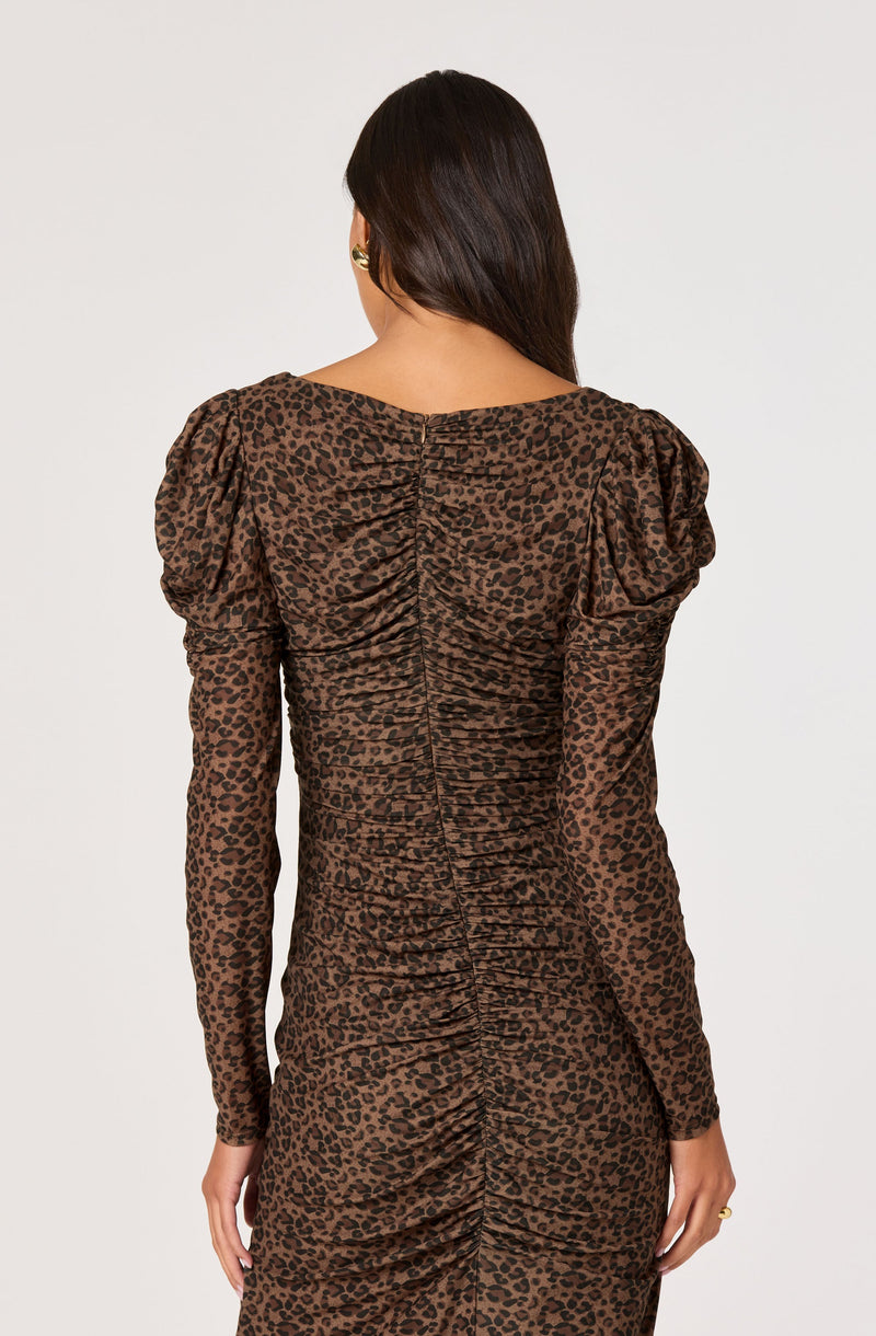 A woman is wearing a fitted, long-sleeved dress with a leopard print pattern. The dress features shoulder puffs and ruched detailing down the back.