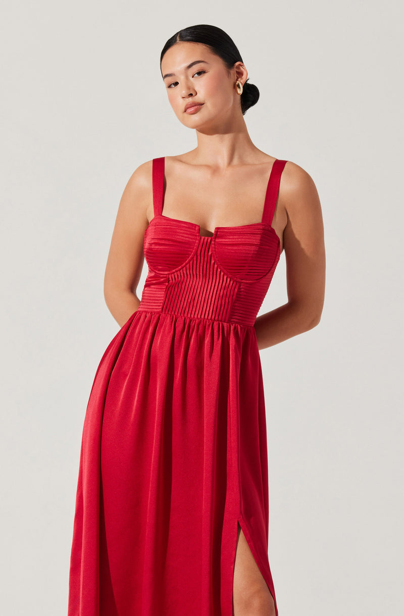 A woman is wearing a red sleeveless dress with wide shoulder straps. The fitted bodice features a textured, ribbed pattern with horizontal and vertical lines, and a central seam that creates a structured look. The skirt is long and flowing, with a high slit on one side, revealing part of her leg.