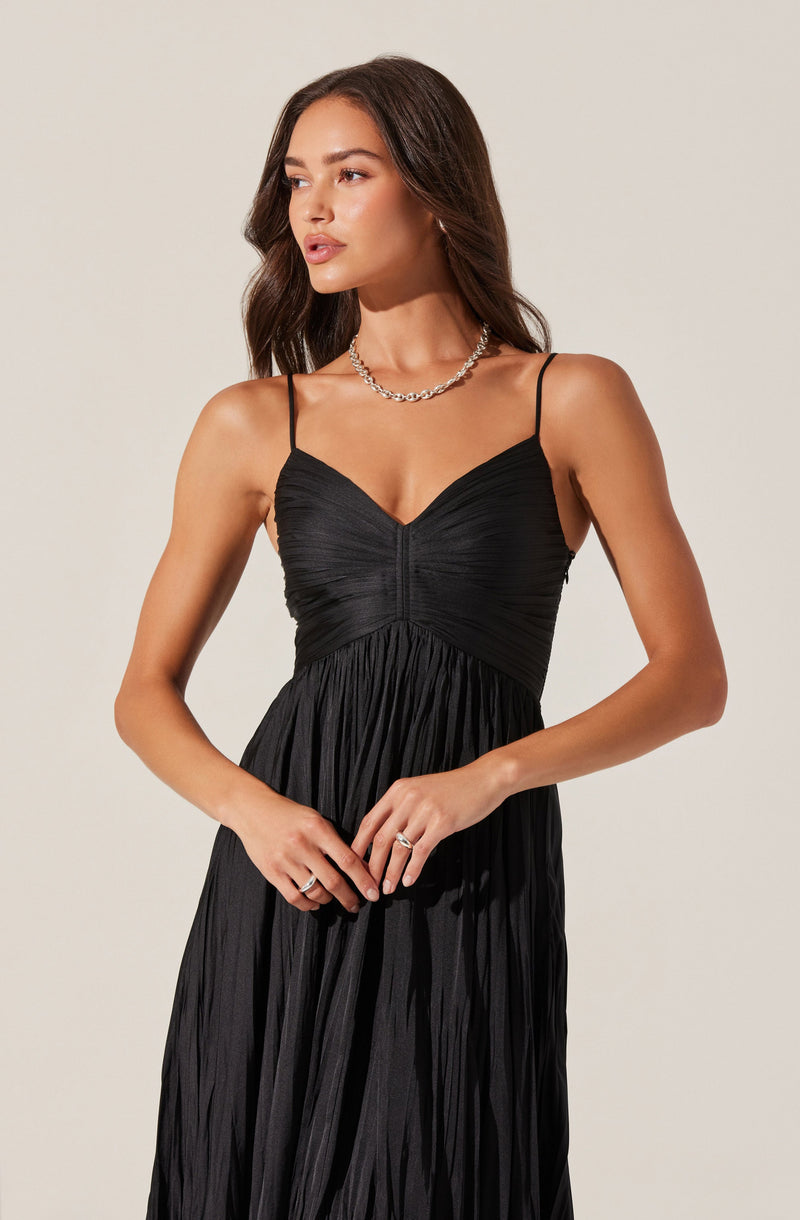 A woman is wearing a black spaghetti strap dress with a fitted, textured bodice and a flowing, pleated skirt. She is accessorized with a chunky silver necklace and a ring on her left hand.