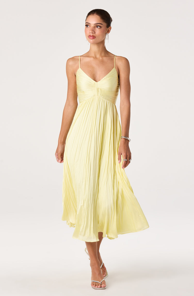 Woman wearing a pale yellow pleated, spaghetti strap dress with a fitted bodice.