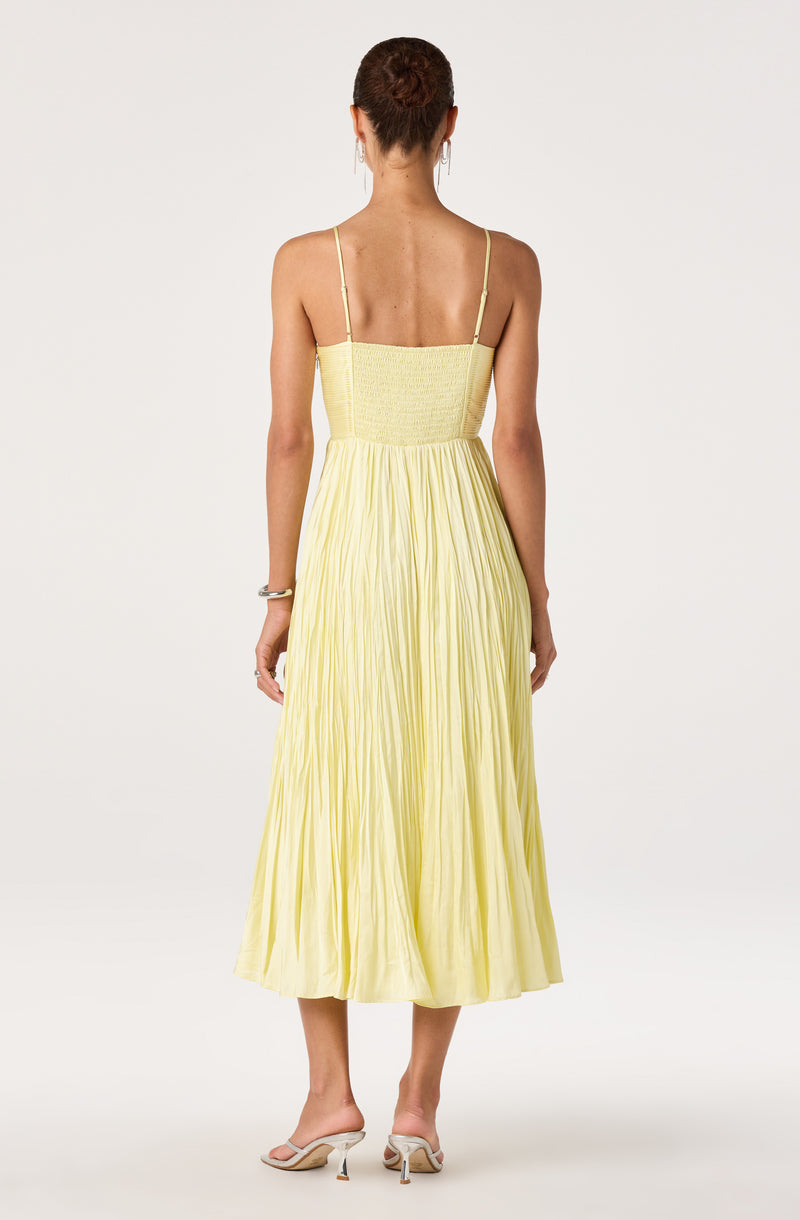 Woman in a light yellow, pleated, sleeveless dress with thin spaghetti straps.