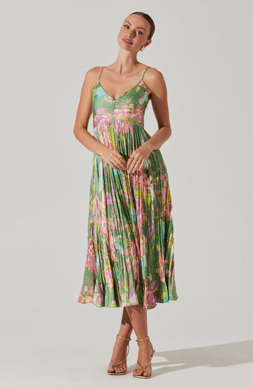 A woman is wearing a sleeveless, V-neck, spaghetti strap dress with a vibrant, multicolored floral pattern. The dress features a fitted bodice and a pleated skirt that falls below the knees. She is also wearing strappy high-heeled sandals.