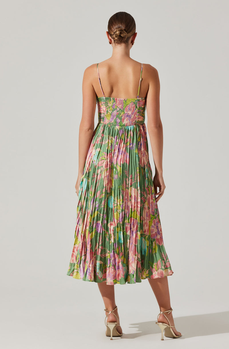 The dress has a fitted bodice with spaghetti straps and a square neckline. The fabric features a colorful floral print with shades of pink, purple, green, and hints of yellow. The skirt is pleated, midi-length, and flows downward, creating a soft, elegant silhouette. The overall look is vibrant and summery.