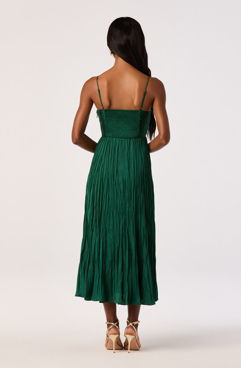 Back view of a woman wearing a green pleated maxi dress with spaghetti straps and nude high heels.
