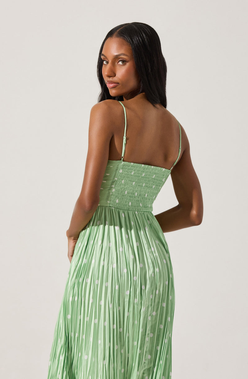 A woman is wearing a light green dress with thin spaghetti straps. The top part of the dress features a smocked, fitted bodice with a subtle dotted pattern. The skirt is pleated, flowing, and has a similar dotted pattern, creating a graceful and elegant appearance.