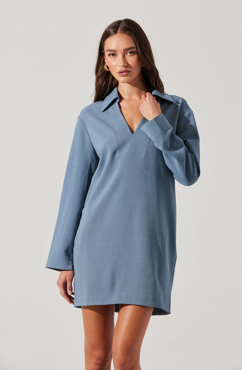 A woman is wearing a loose-fitting, light blue dress with long sleeves. The dress features a pointed collar and a hemline that falls above the knees. The fabric appears to be smooth and slightly textured.