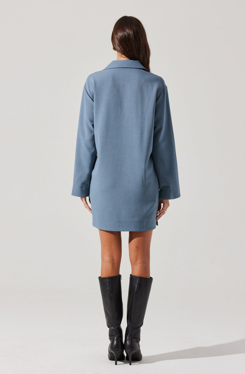 A woman is wearing a light blue, long-sleeved shirt dress with a collar, paired with tall black leather knee-high boots with pointed toes and high heels.