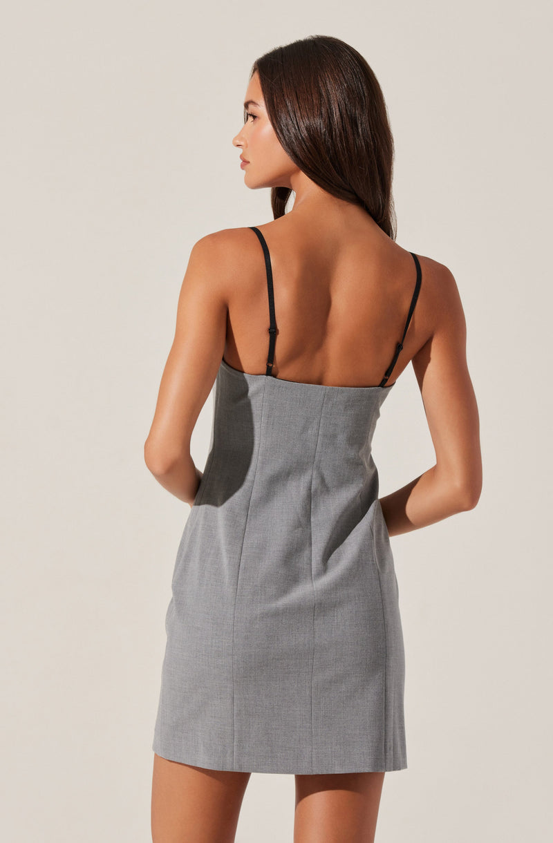 A woman is wearing a sleeveless, fitted dress with thin black spaghetti straps. The dress is light gray with a subtle checkered pattern and has a high waistline. The fabric appears to be a structured material, and the dress falls above the knee. She has long, straight brown hair and is shown from the back, standing against a plain, light background.