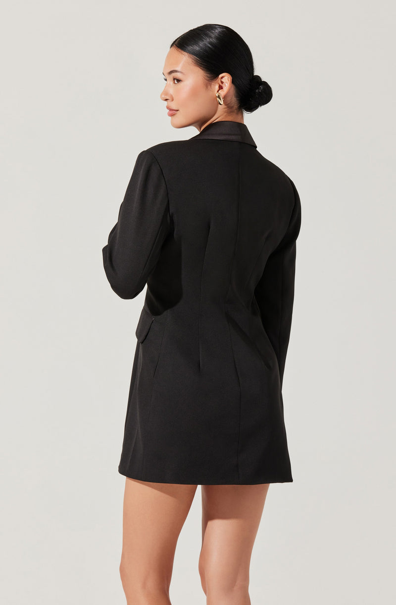A woman is wearing a fitted, long-sleeved black blazer dress with a collar.