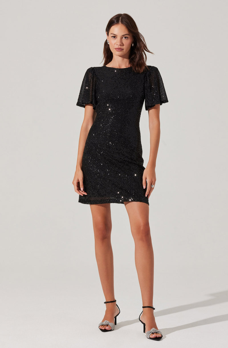 A woman is wearing a short black sequined dress with puffed sleeves and a round neckline. She has on black and silver high-heeled sandals with ankle straps.