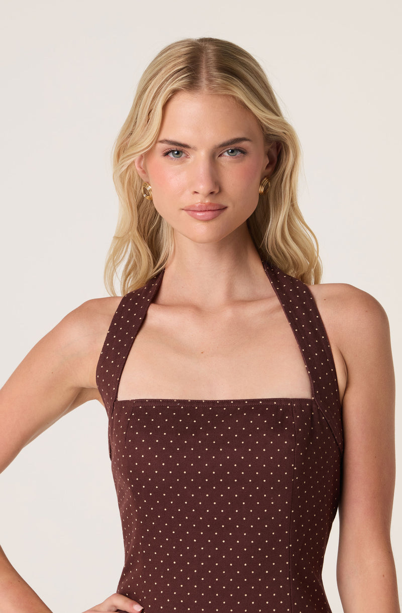 Woman in brown polka dot sleeveless dress with halter neckline and gold earrings.