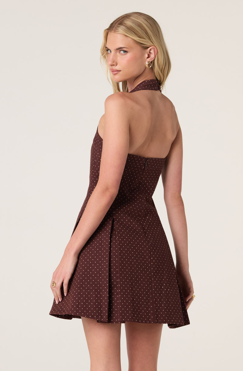 Woman in a sleeveless, halter-neck brown dress with small white polka dots and a flared skirt.