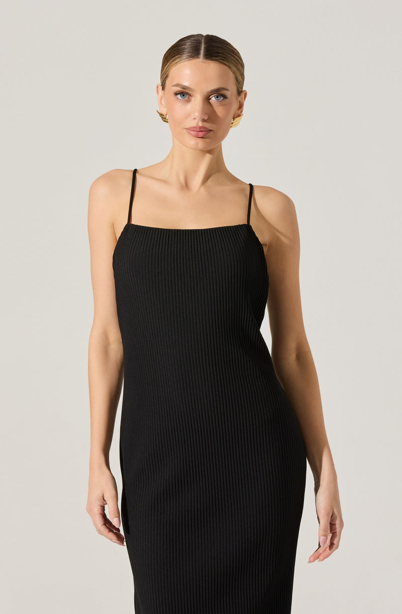 A woman is wearing a form-fitting, sleeveless black dress with thin spaghetti straps. The dress features a vertical ribbed texture throughout.