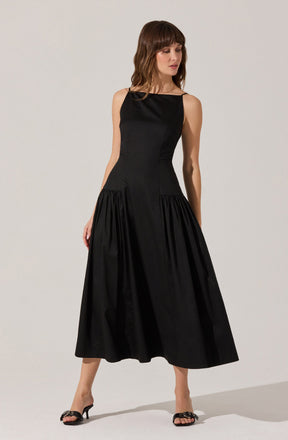 A woman is wearing a sleeveless, ankle-length black dress with a fitted bodice and a full, gathered skirt. She has on black high-heeled sandals with decorative bows on the front.
