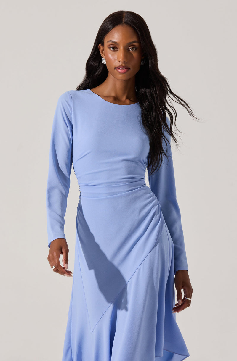 A woman is wearing a long, light blue dress with long sleeves. The dress has a fitted bodice with ruching details at the waist and a flowing skirt with draped fabric.