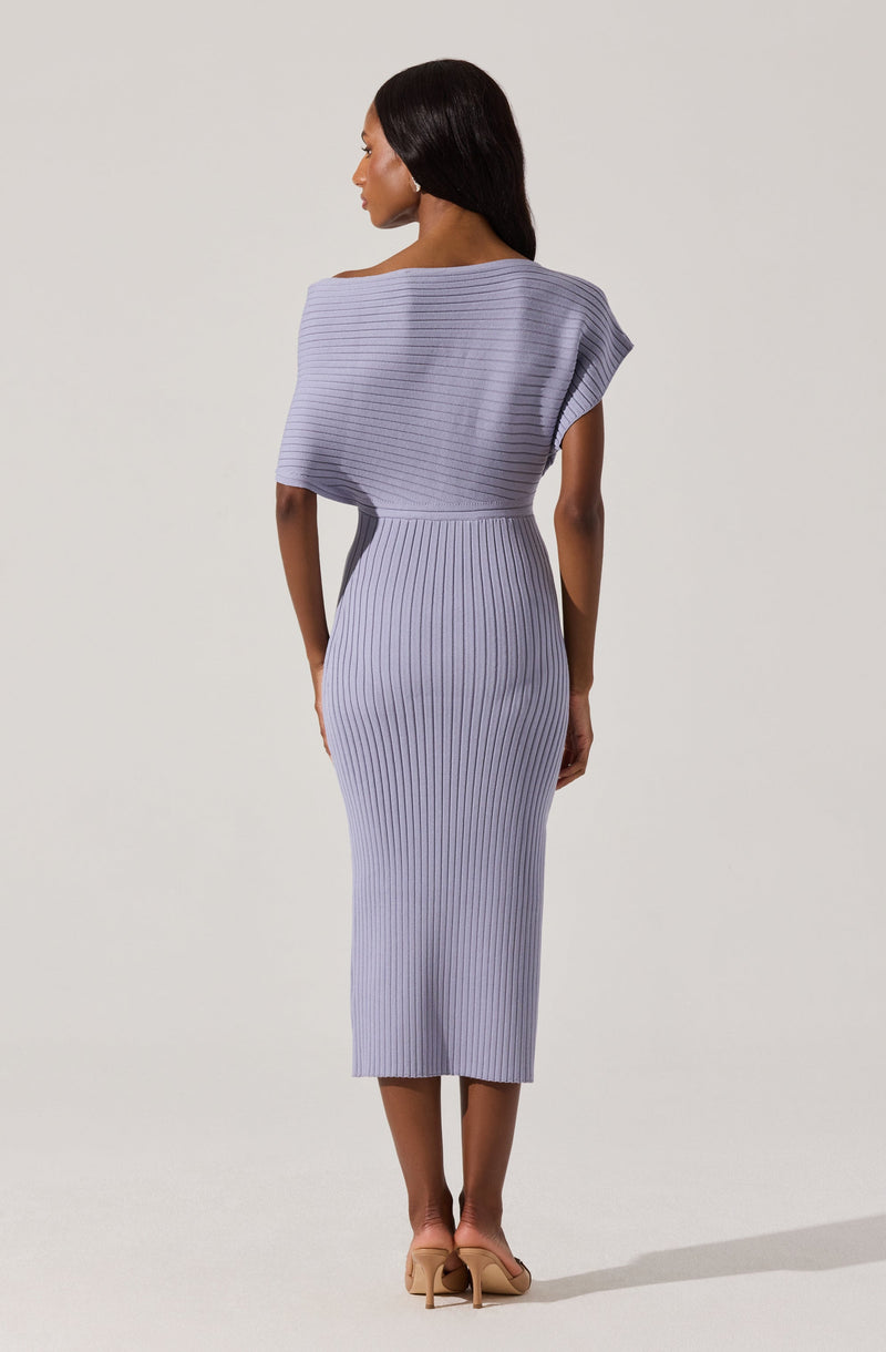 A woman is wearing a form-fitting, ribbed knit dress in a soft lavender color. The dress features a high waist and a midi length, ending just above the ankles. The top part of the dress has an asymmetrical, layered design with a wide, off-the-shoulder neckline, creating a draped appearance on one side. The fabric has horizontal ribbing on the top and vertical ribbing on the skirt, adding texture to the outfit.