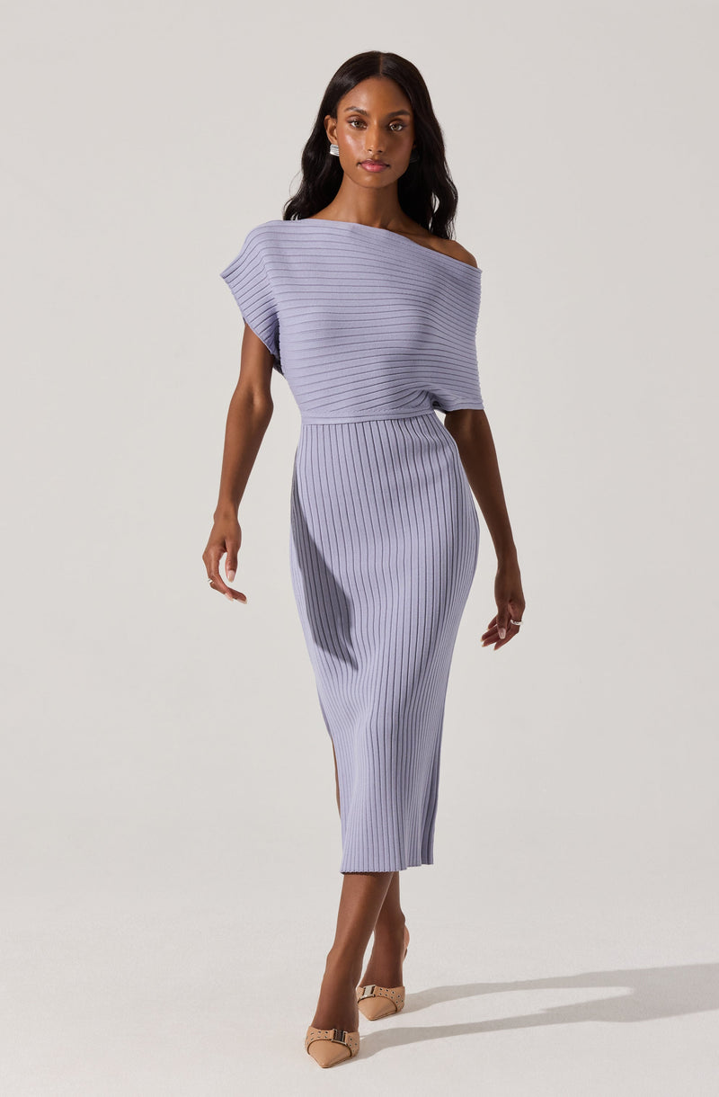 A woman is wearing a light purple, off-the-shoulder dress with thin, vertical striped patterns. The dress has a loose, draped top with short sleeves, and a fitted, high-waisted skirt that extends to mid-calf length. She is also wearing beige high-heeled shoes with decorative embellishments.