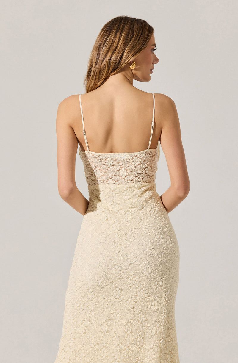 A woman is wearing a sleeveless dress with thin spaghetti straps. The top part of the dress features a lace overlay, while the lower part appears to be made of a textured, possibly embroidered fabric. The dress is form-fitting and in a light, neutral color.