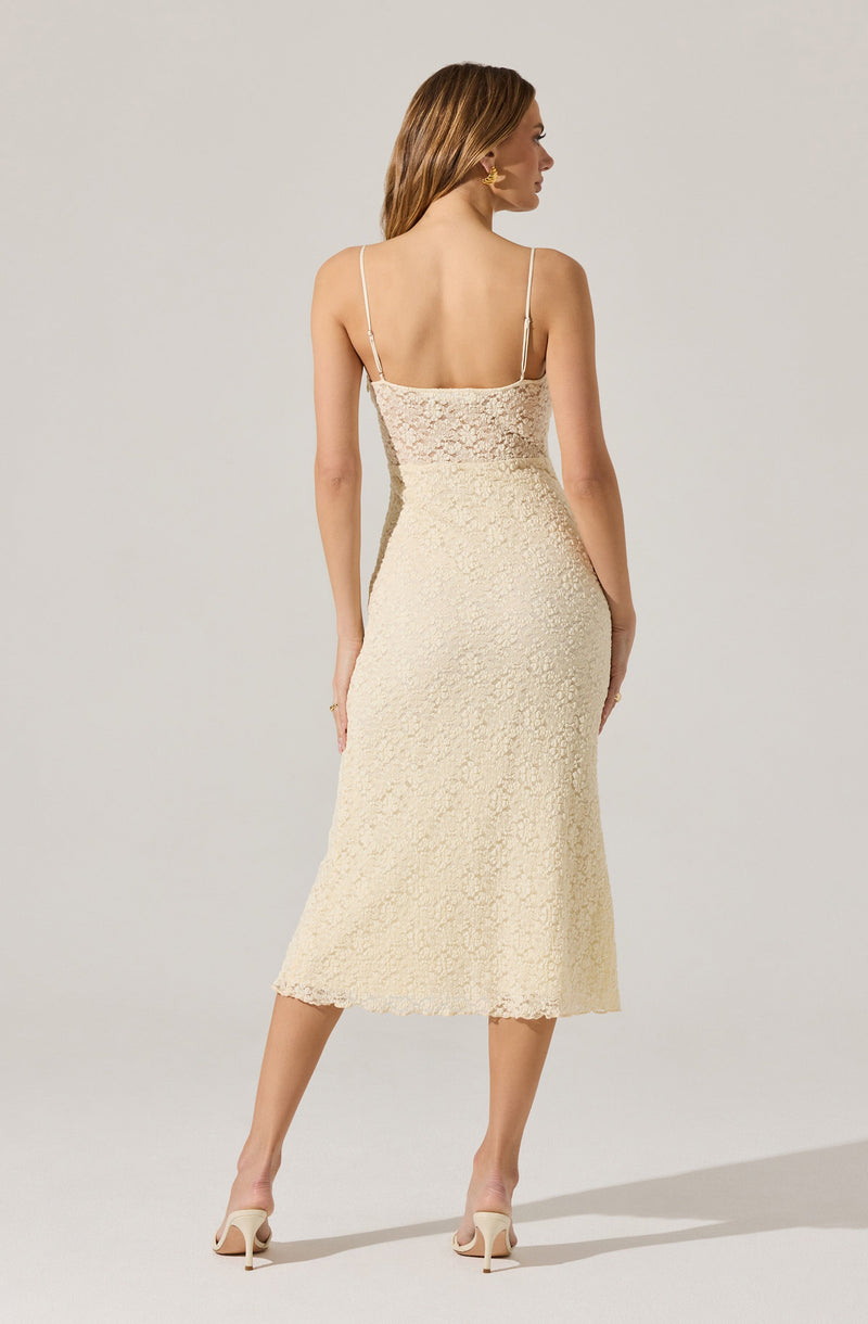 A woman is wearing a cream-colored, textured, sleeveless dress with thin spaghetti straps. The dress has a fitted silhouette that extends to mid-calf length. She is also wearing light-colored high-heeled shoes.