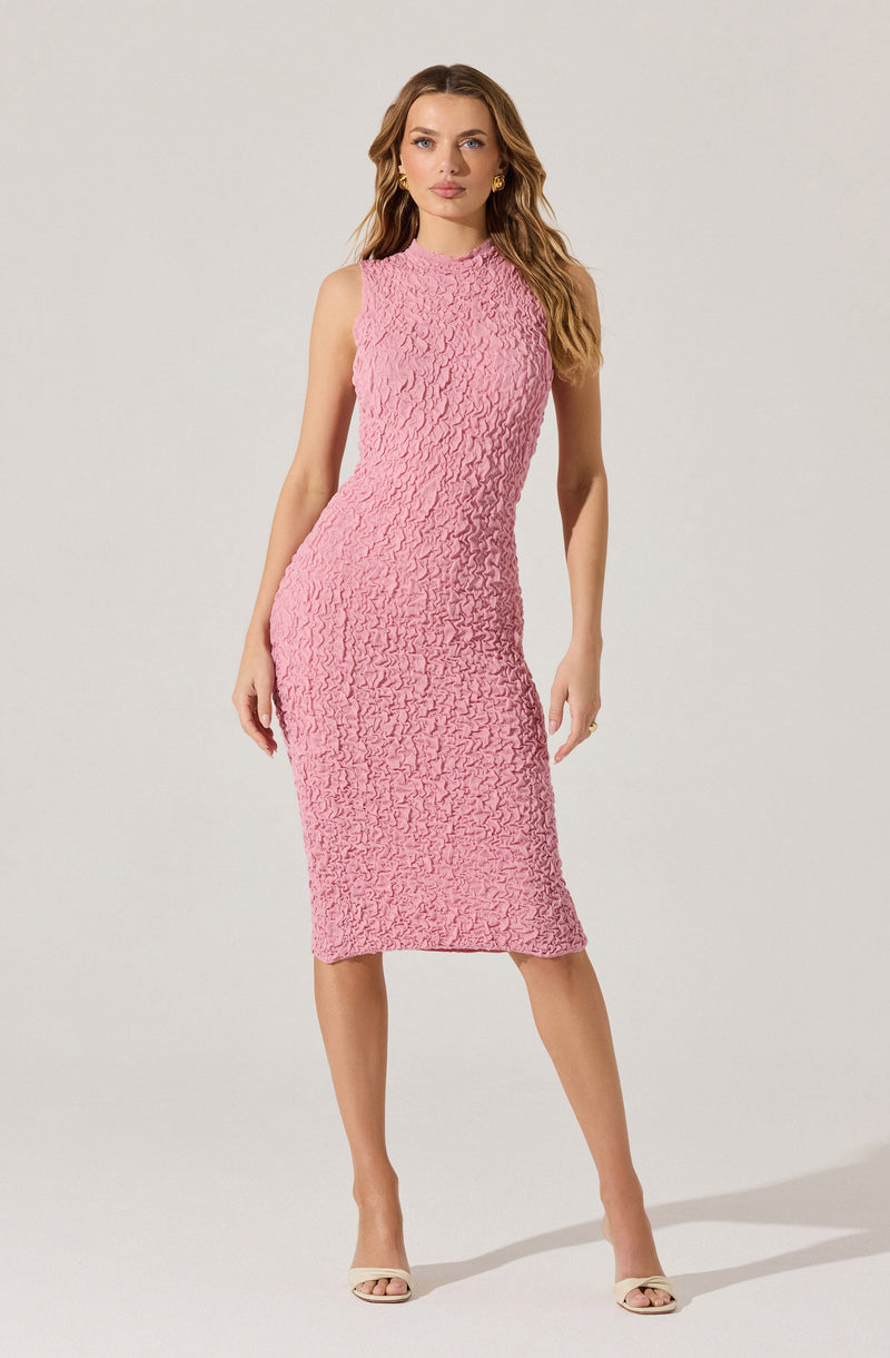 A woman is wearing a sleeveless, knee-length pink dress with a textured, crinkled fabric pattern. She has on beige open-toe heels and gold hoop earrings.