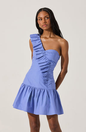 The dress is a light blue mini dress with a strapless, sweetheart neckline. It features a single ruffle strap that runs from the front to the back on the left shoulder, with tailored ruching along the bust and midsection. The dress has a fitted waist and a gathered, flared skirt at the hem.
