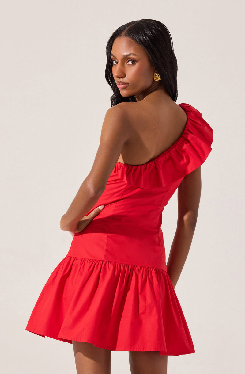 A woman is wearing a bright red, one-shoulder dress with a ruffled neckline and a gathered skirt. The dress has a fitted bodice and a ruffled hemline that falls above the knees.