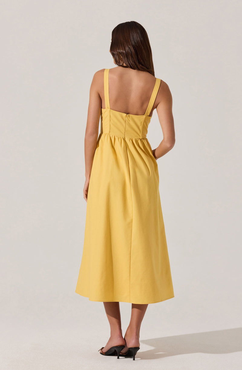 A woman is wearing a sleeveless, yellow dress with wide straps, fitted at the waist, and a full, mid-calf length skirt. She is also wearing black high-heeled sandals.
